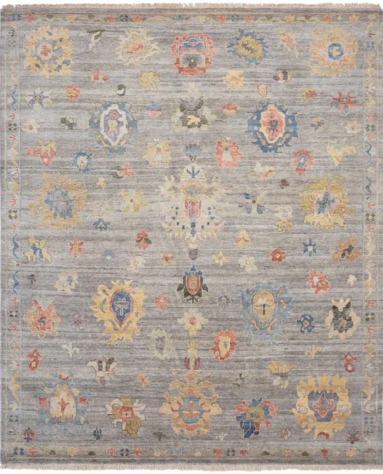 Top-down studio shot of a traditional area rug with a pearl grey field and scattered floral medallions in shades of coral, azure blue, and mustard yellow.